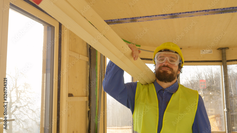 CLOSE UP: Man carrying planks across a beautiful wooden house under construction