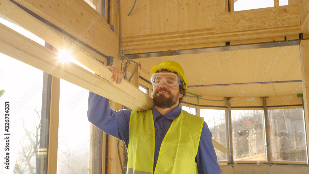 CLOSE UP: Worker arrives to work carrying heavy wooden beams on his shoulder