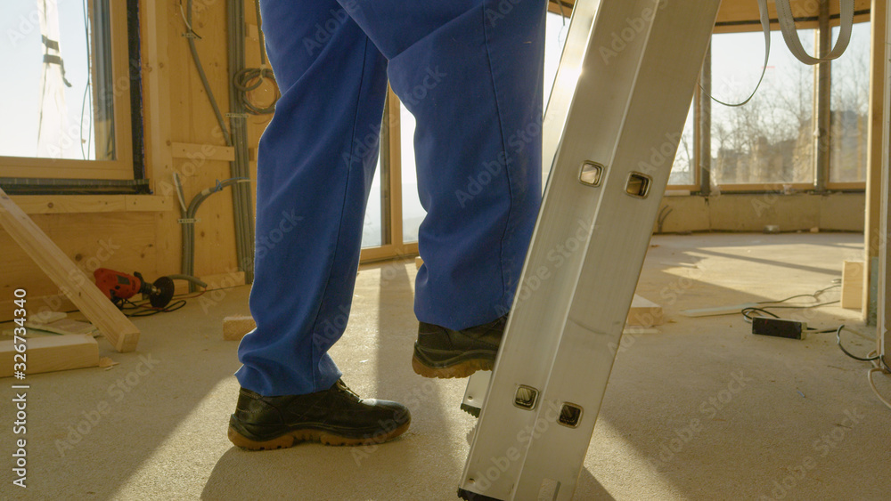 CLOSE UP: Close up shot of workers legs as he climbs up an aluminium ladder.