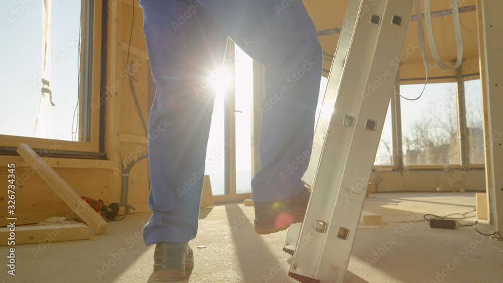 LENS FLARE: Morning sunrays shine on worker climbing up an industrial ladder.