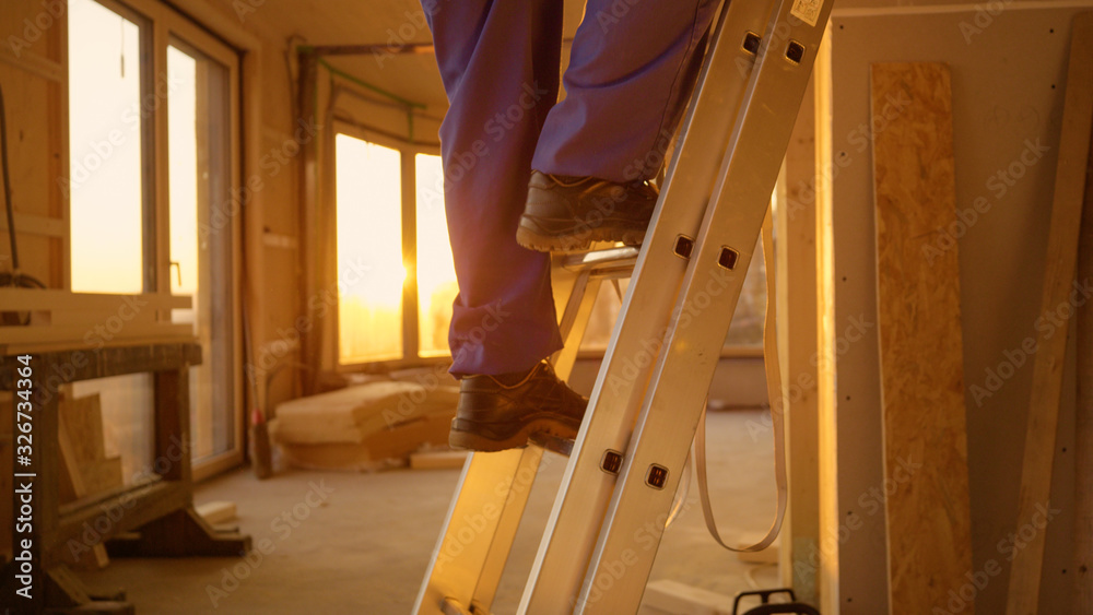 LENS FLARE: Builder in blue overalls climbs down a aluminium ladder at sunset.