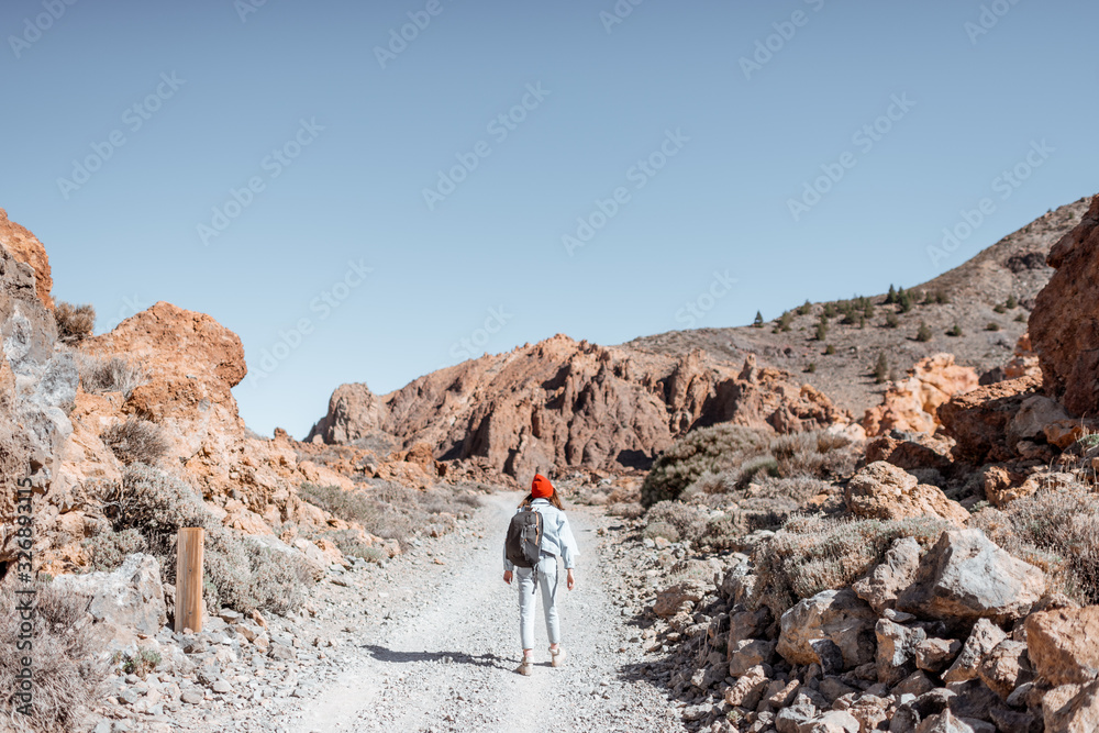 火山谷上风景如画的岩石地形和土路。年轻的女旅行者走在上面