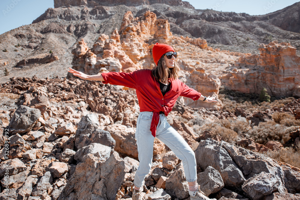 Young woman dressed casually in red shirt and hat walking on the rocky terrain on a sunny day. Trave