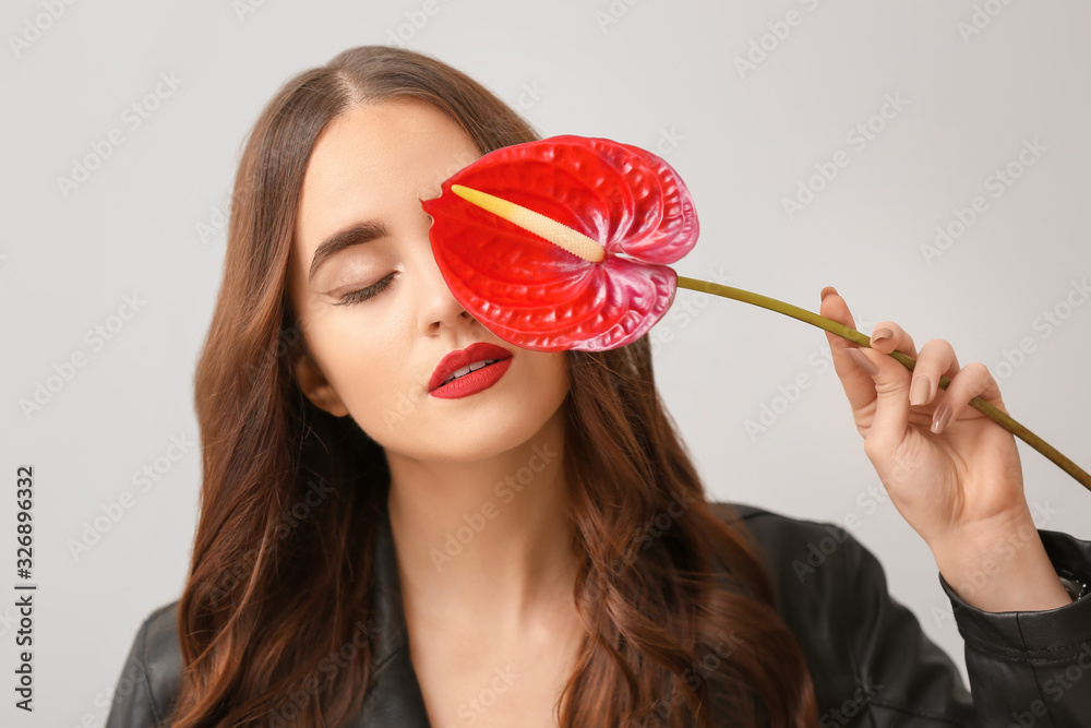 Beautiful young woman with long hair and flower on light background