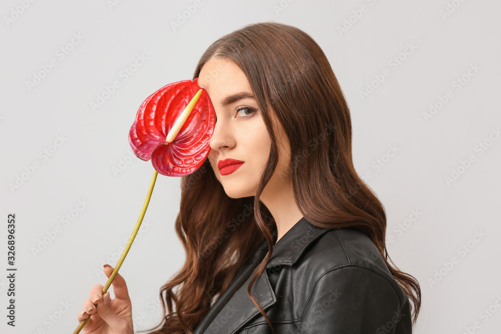 Beautiful young woman with long hair and flower on light background