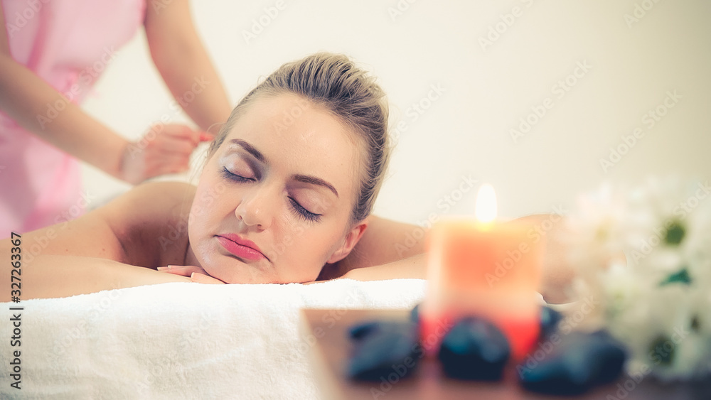 Massage therapist holds a herbal compress to do treatment to woman lying on spa bed in a luxury spa 