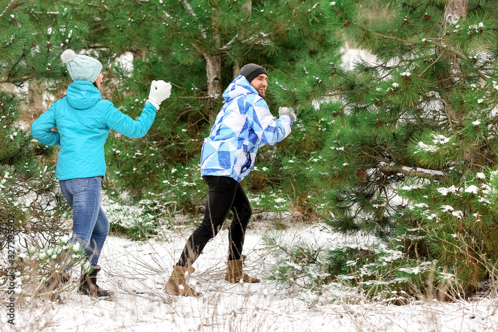 Happy young couple playing snowballs in park on winter day