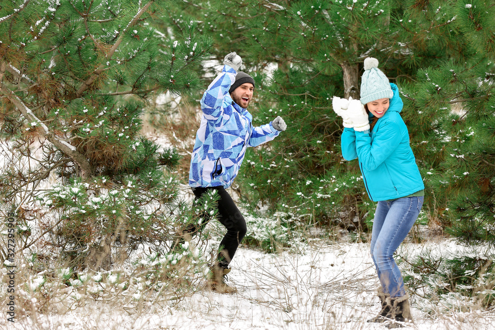 Happy young couple playing snowballs in park on winter day