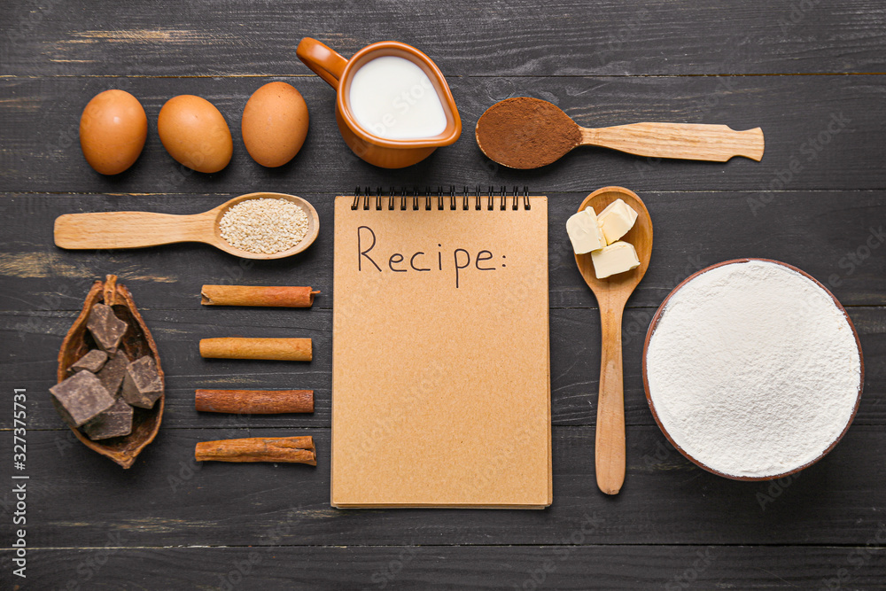 Ingredients for preparing bakery and notebook on dark wooden background