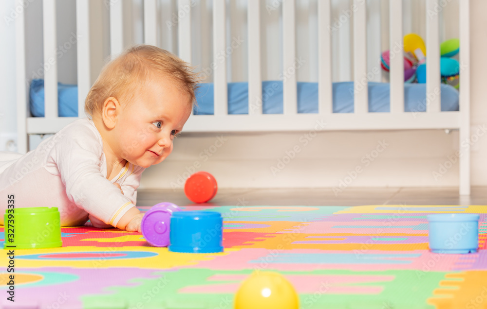 Baby toddler boy creep on the floor of nursery playing with colorful toys