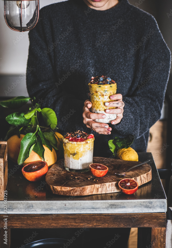 Young woman holding glass of overnight oat bircher muesli with mango smoothie, buckwheat granola and