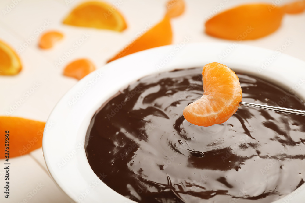 Bowl with tasty chocolate fondue and tangerine piece on table, closeup