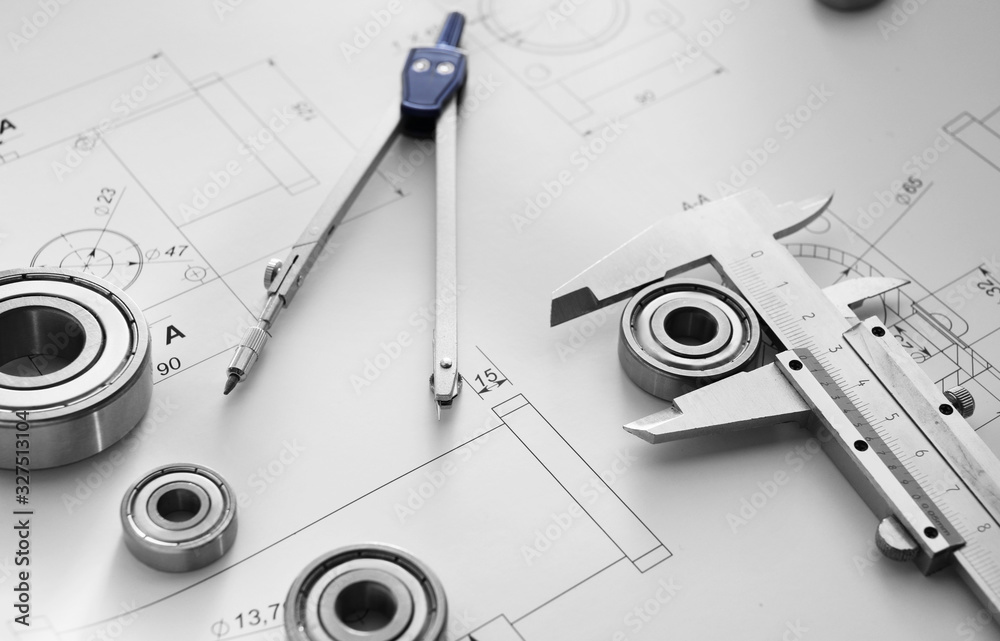 Bearings with pair of compasses, vernier caliper and drawings on table of engineer