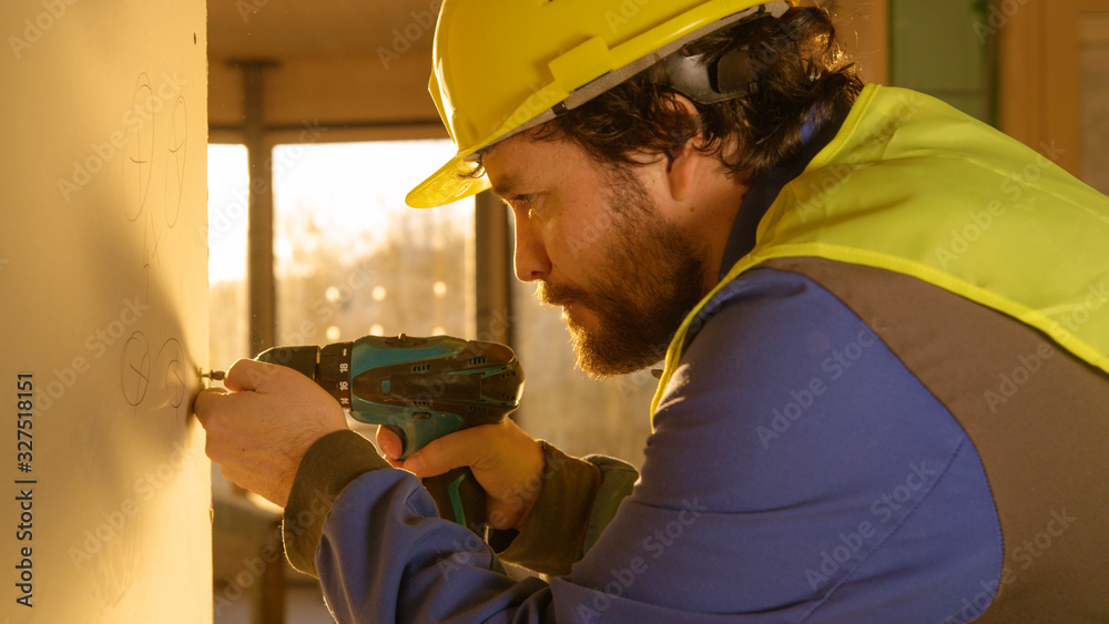 CLOSE UP: Contractor wearing a hard hat uses a power drill to mount a wall panel