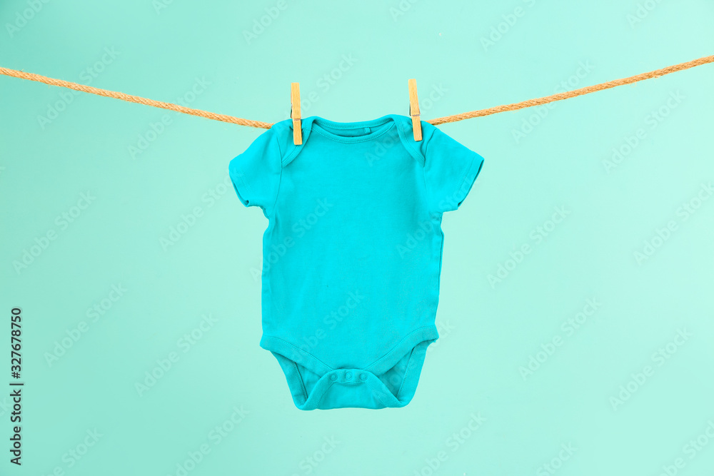 Baby clothes hanging on rope against color background