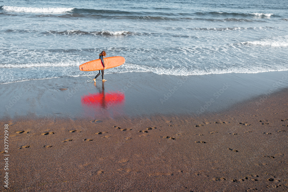 Beautiful sunset view on the ocean beach and surfer walking with red surfboard on a sunset