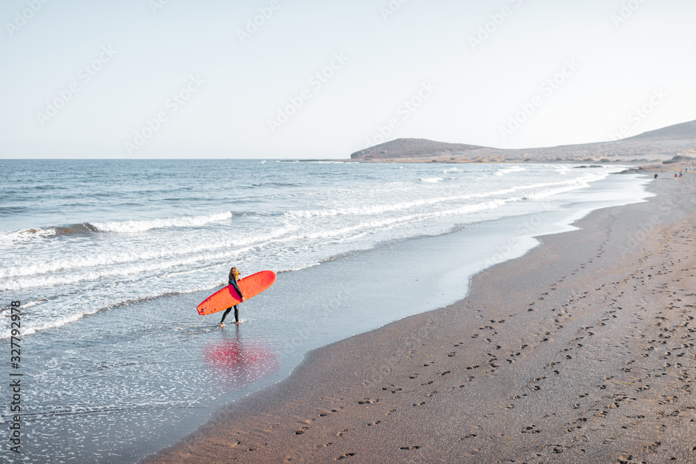 Beautiful sunset view on the ocean beach and surfer walking with red surfboard on a sunset