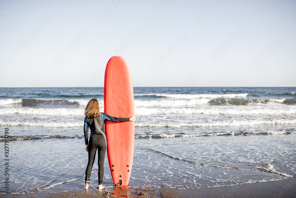 Surfer enjoying beautiful seascape, standing with surfboard on the ocean beach during a sunset, view