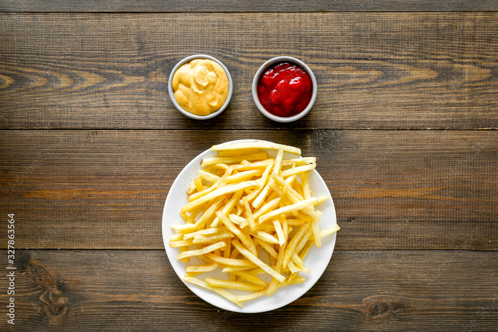 Fast food symbol. French fries on plate on dark wooden table top-down copy space