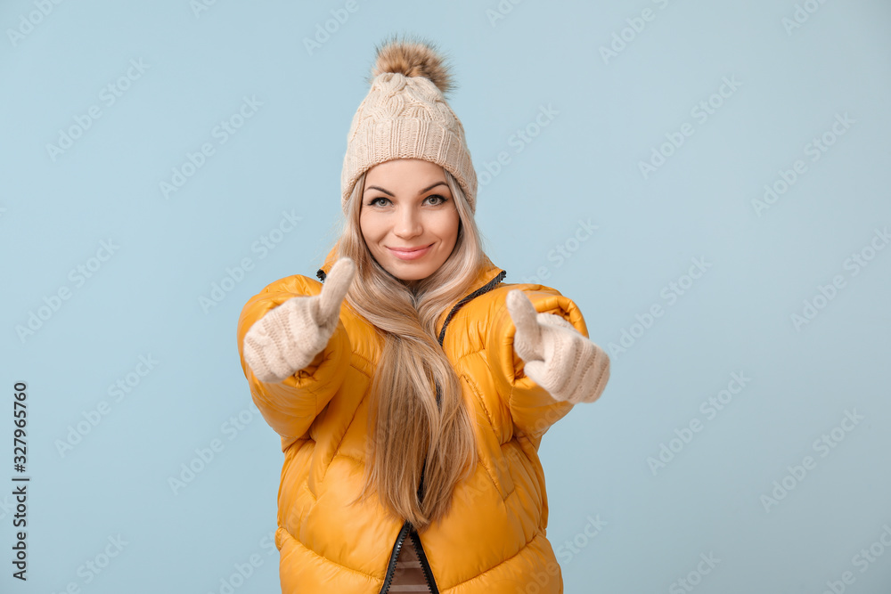 穿着冬装的漂亮年轻女子在彩色背景上展示拇指向上的姿势