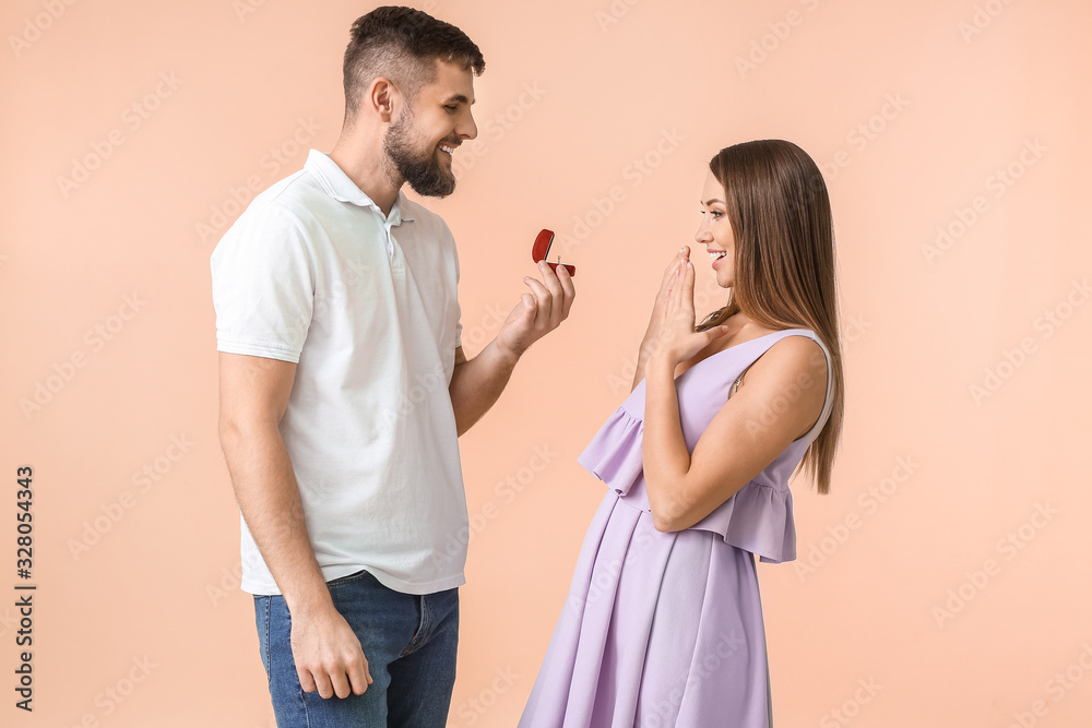 Young man proposing to his beloved on color background