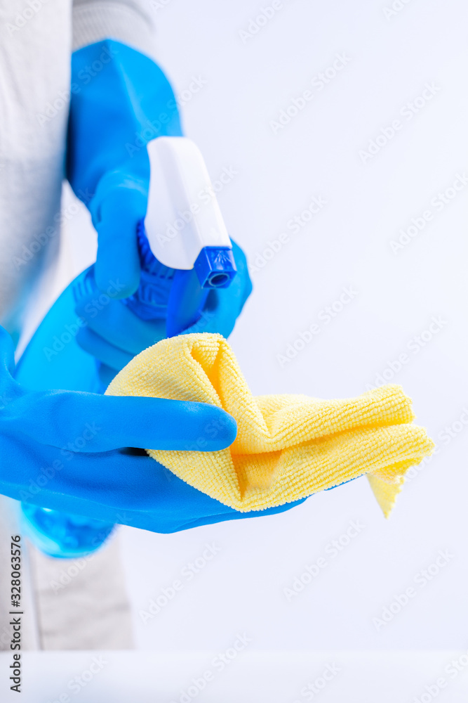 Young woman housekeeper is doing cleaning white table in apron with blue gloves, spray cleaner, wet 