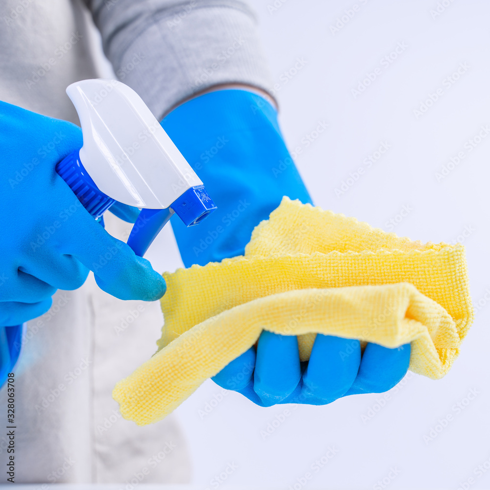 Young woman housekeeper is doing cleaning white table in apron with blue gloves, spray cleaner, wet 