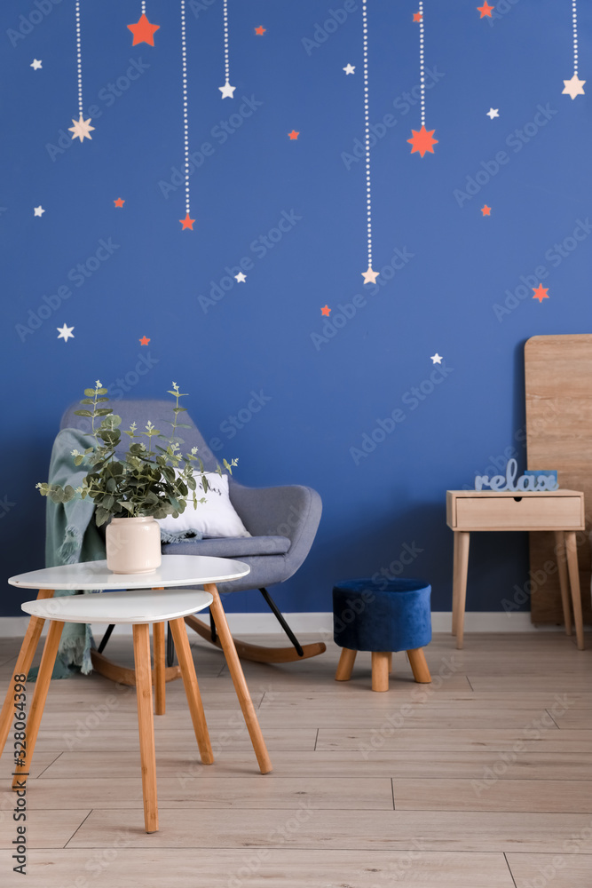 Stylish interior of room with armchair and table near blue wall