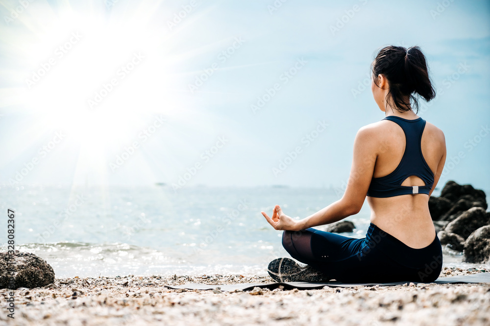 Young Asian woman practicing yoga exercise at quiet rock pier with sea background. Sport and recreat