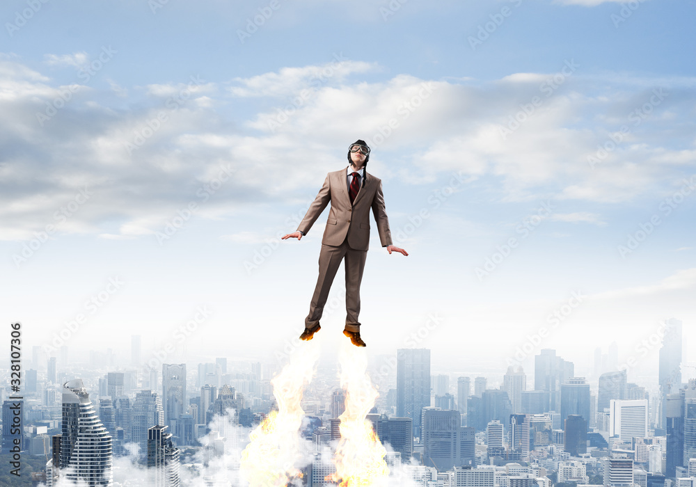 Businessman in suit and aviator hat flying in sky