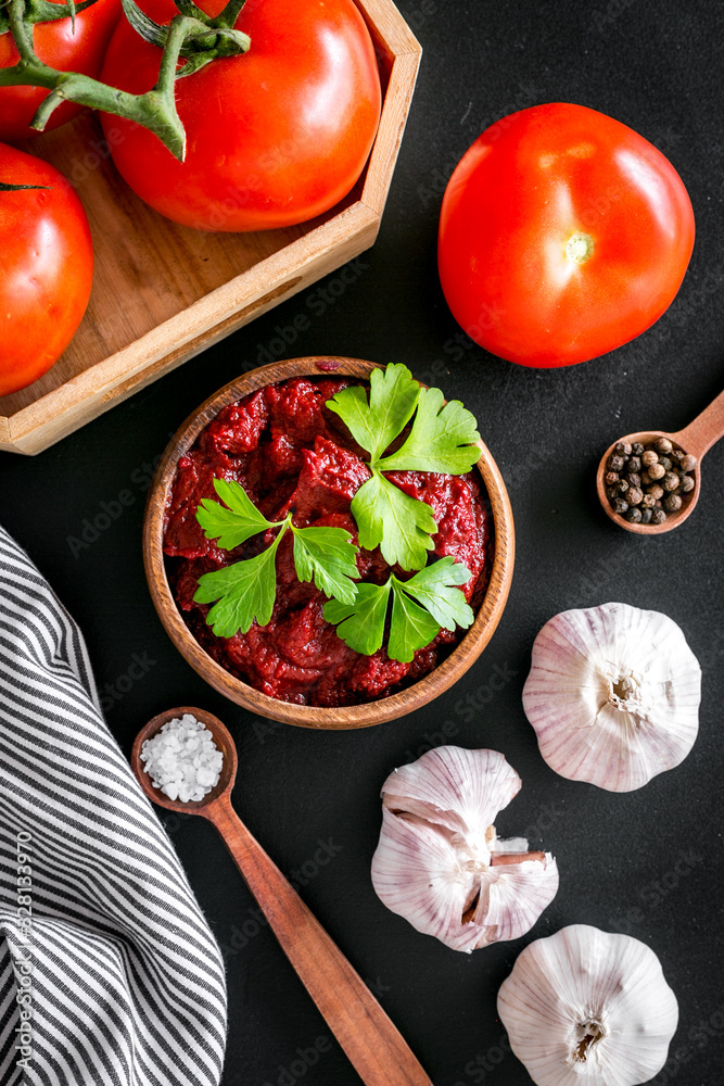 Homemade tomato sause near ingredients - garlic, spices - on black background top-down