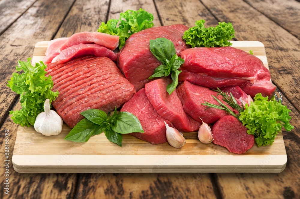 A heap of raw meat with garlic and greens on wooden board