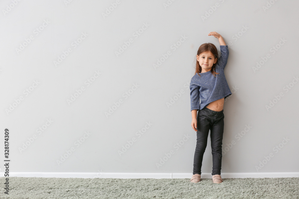 Little girl measuring height near grey wall