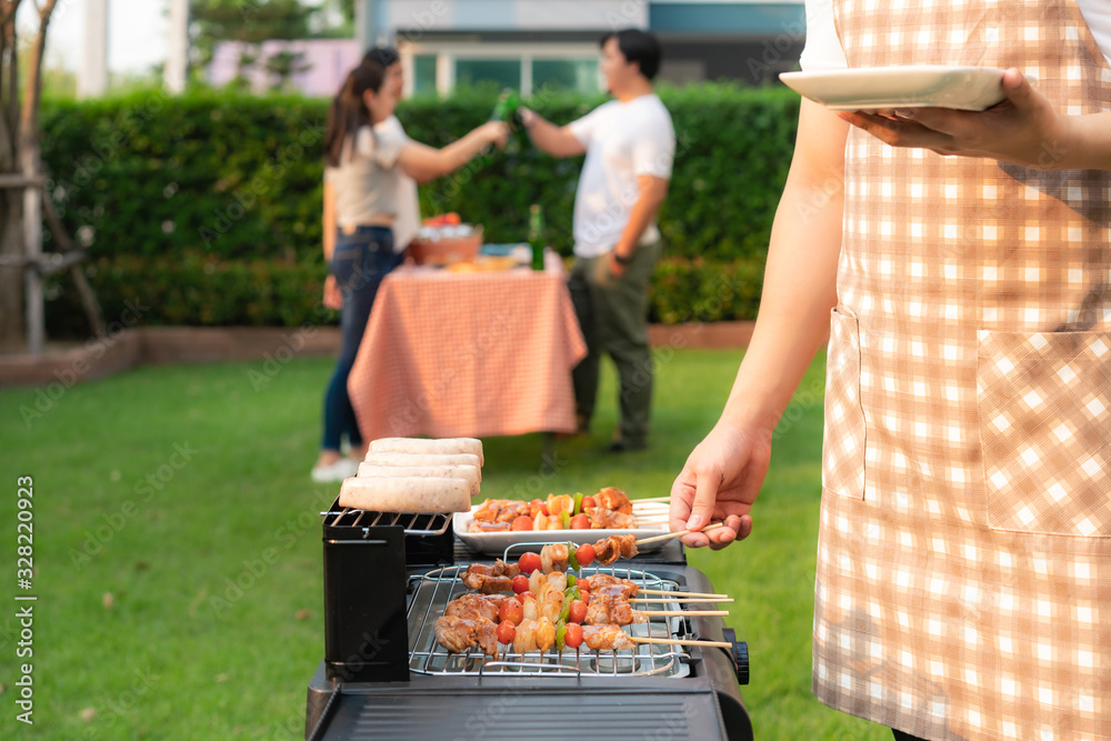 Asian man cooking barbeque grill and sausage for a group of friends to eat party in garden at home. 