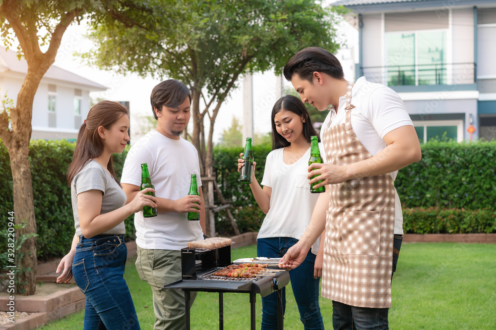 Asian man cooking barbeque grill and sausage for a group of friends to eat party in garden at home. 