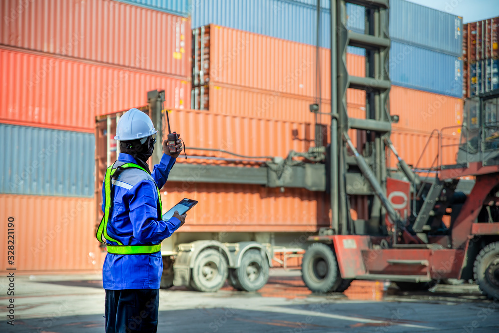 Foreman using and talking walkie talkie to control loading Containers box to truck at Container depo