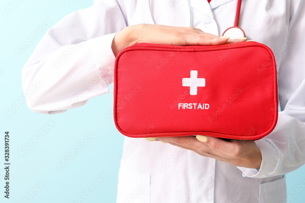 Female paramedic with first aid kit on color background, closeup