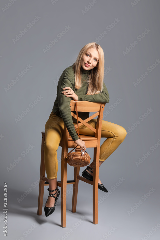 Young woman in warm sweater and with stylish bag on grey background