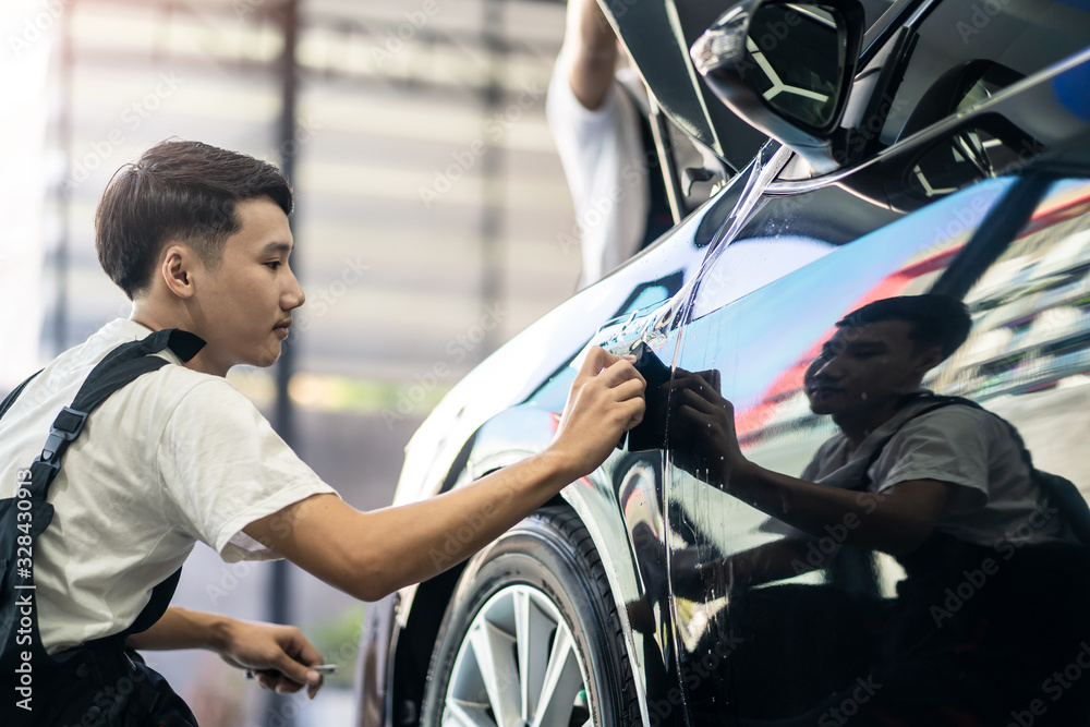 Two Asian car film protection male worker installing film to black color car in garage. Man focus ho