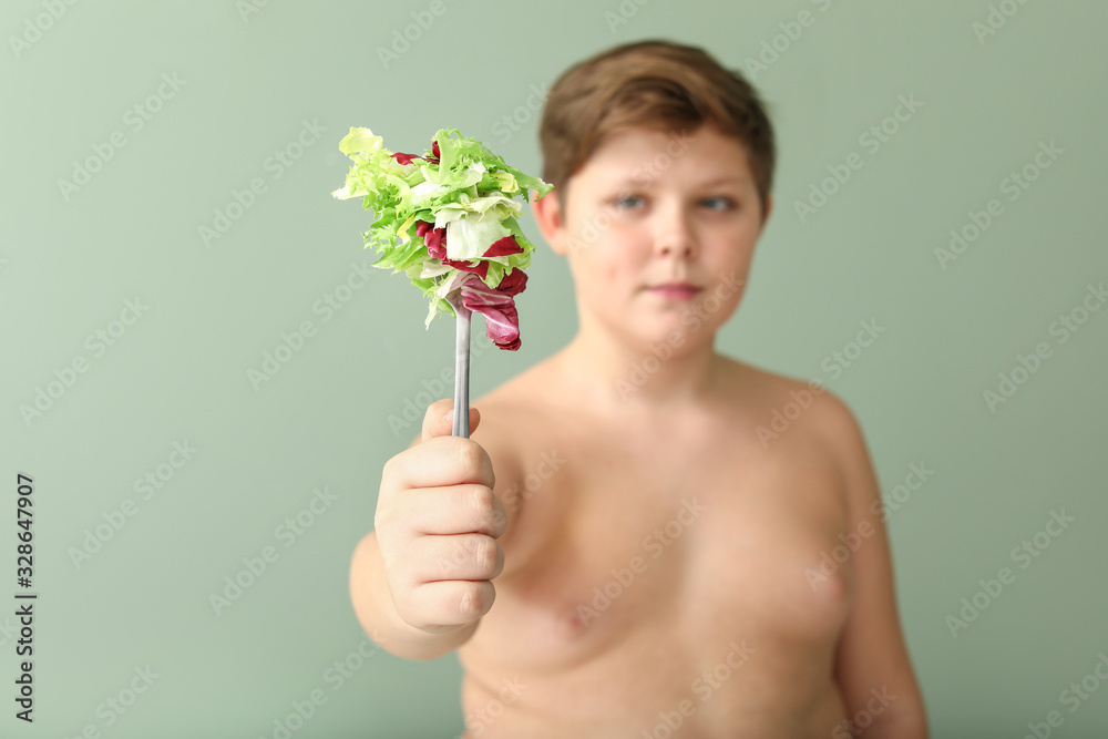 Overweight boy with salad on color background