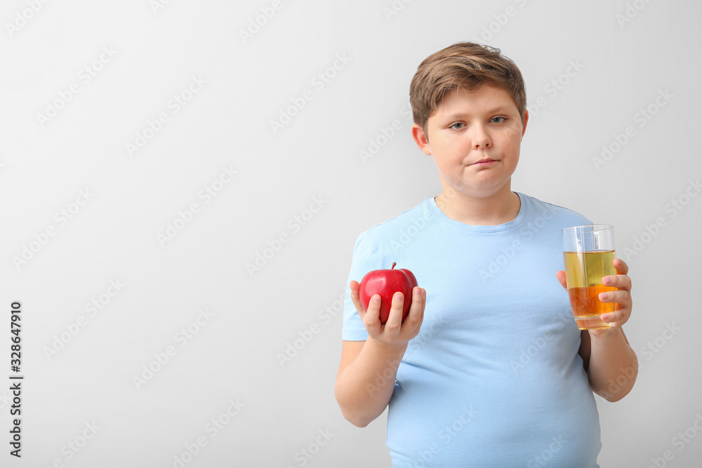 Overweight boy with apple and juice on light background