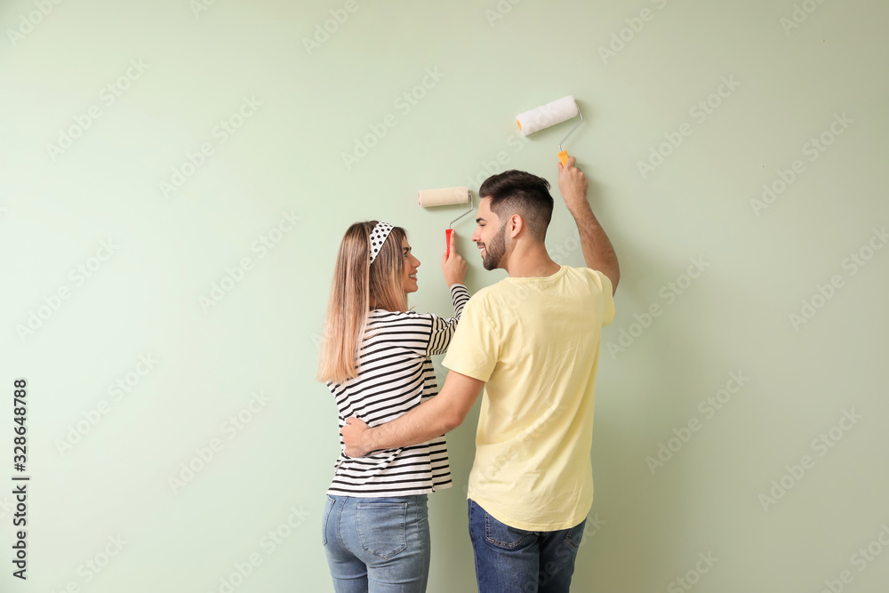 Happy young couple painting wall in their new house