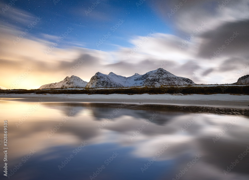 Mountains and reflections on water at night. Winter landscape. The sky with stars and clouds in moti