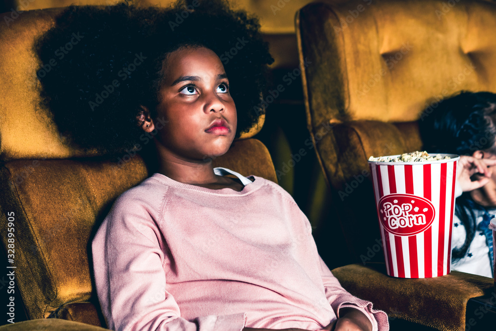 Two children african and asian having fun and enjoy watching movie in cinema