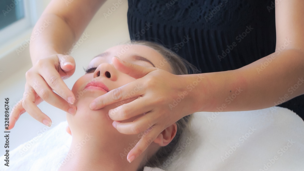 Relaxed woman lying on spa bed for facial and head massage spa treatment by massage therapist in a l