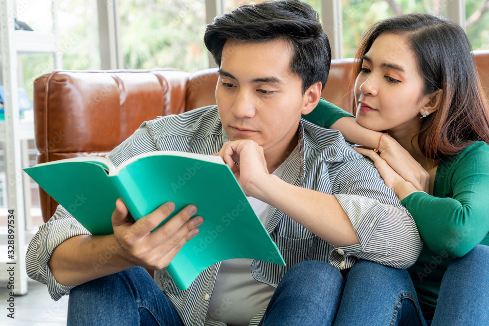 Young Asian couple reading book in living room. Love relationship and lifestyle concept.