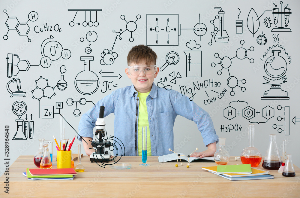 Cute little boy studying chemistry at table against grey background