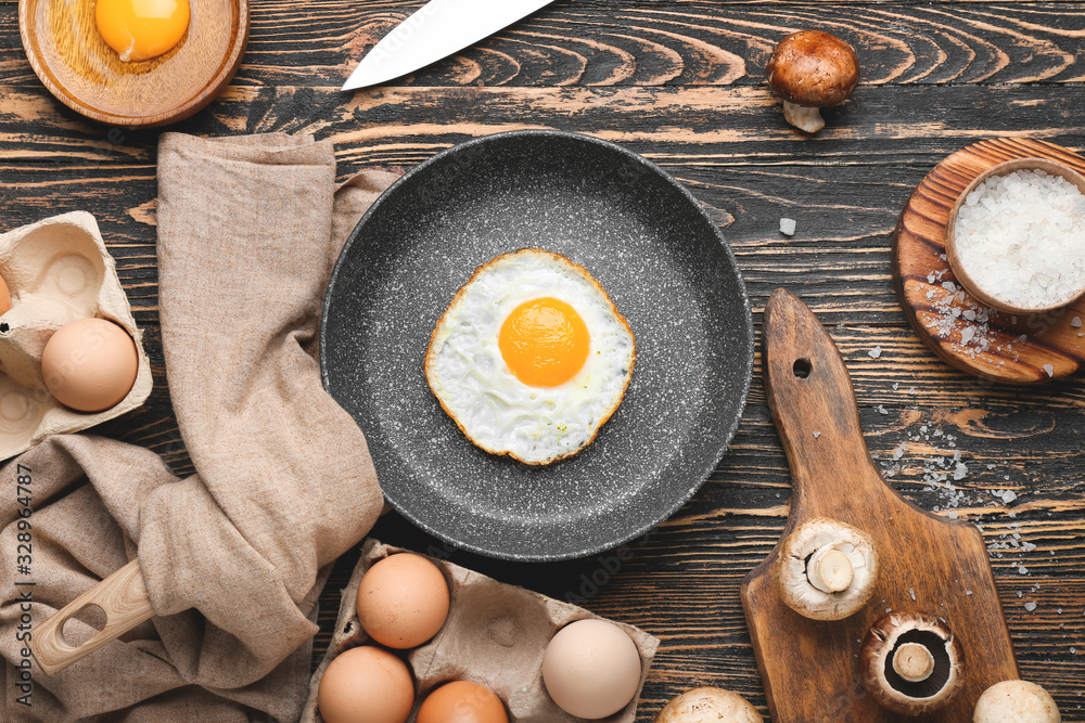 Frying pan with cooked and raw eggs on wooden background