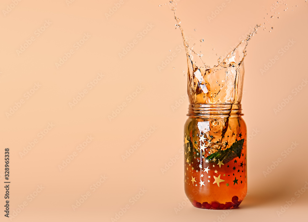 Mason jar of cold tea with splashes on color background