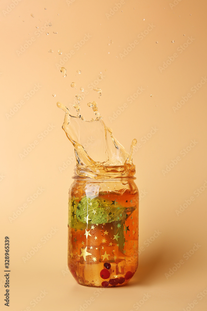 Mason jar of cold tea with splashes on color background